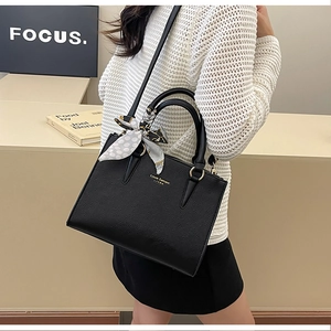 Structured black leather handbag with polka dot scarf and gold strap details