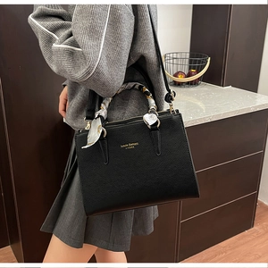 Detail of black pebbled leather handbag with gold hardware and decorative silk scarf handle
