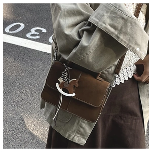 Detail of a brown crossbody bag with a white horse charm in a stylish street setting