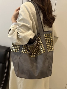 Sac fourre-tout gris en similicuir à clous dorés porté par un mannequin en trench beige