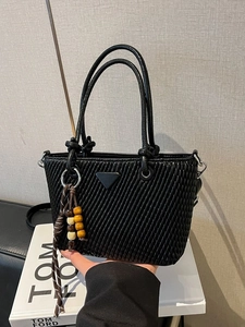 Quilted black bucket bag with a metal triangle logo and beaded charm on a Tom Ford book