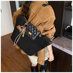 Detail of black suede tote bag with quilted pocket and gold chain strap on a model