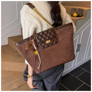 Detail of a large brown suede tote bag with chain strap and heart pendant accessory