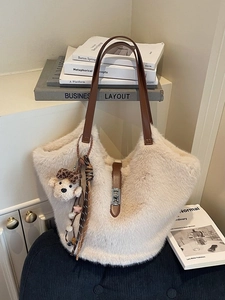Sac fourre-tout en peluche crème avec anses en cuir marron et pendentif ours sur une chaise