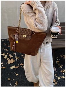 Close-up of brown suede tote bag featuring diamond quilted pocket and gold chain strap