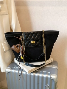 Fashionable black tote bag with gold chain strap and heart charm on silver suitcase