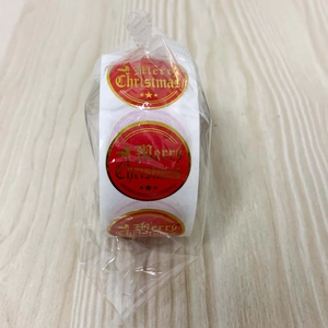 Macro shot of gold foil Merry Christmas stickers on a red roll with star accents