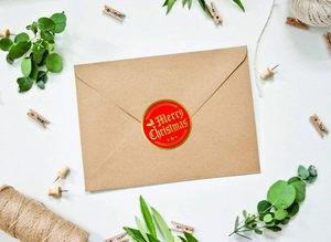Red Merry Christmas sticker with gold foil lettering on a brown kraft envelope