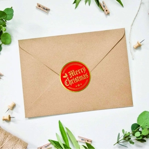 Red Merry Christmas stickers with gold foil lettering on a kraft paper envelope