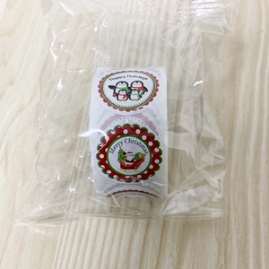 Roll of round Christmas stickers with Santa and penguin motifs on a wooden background