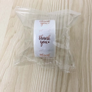 Macro detail of round white thank you stickers with rose gold foil lettering in a roll