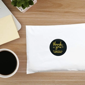 Black round small business thank you stickers on white poly mailer with office supplies