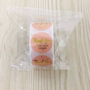 Close-up of pink and gold foil 'Thank You' sealing stickers on a roll in plastic packaging