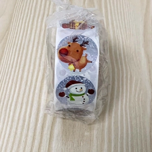 Detail of Christmas sticker roll showing cartoon reindeer and snowman designs on wood surface