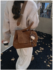 Dettaglio borsa tote in pelle scamosciata marrone scuro con tracolla larga e ciondolo