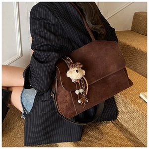 Dettaglio di una borsa tote in pelle scamosciata marrone con ciondolo a forma di orso