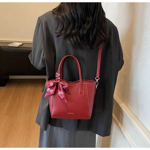 Dettaglio della borsa tote in pelle rossa con logo e foulard di seta sulla spalla