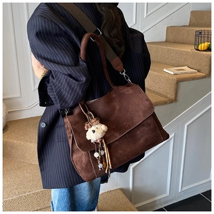 Dettaglio borsa tote in pelle scamosciata marrone scuro con ciondolo orsetto su blazer