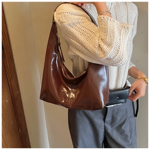 Detail of dark brown glossy patent leather shoulder bag with wide strap on model
