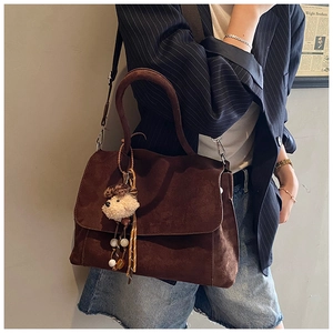 Dettaglio borsa tote in pelle scamosciata marrone con ciondolo su modella in blazer