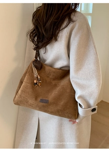 Detail of a large vintage brown suede tote bag with heart charm and tassel on model