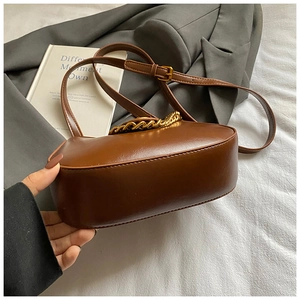 Gros plan du sac croissant marron avec chaîne dorée sur fond minimaliste et élégant