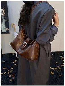 Detail view of large dark brown leather shoulder bag with metallic buckle and wide strap