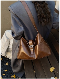 Brown leather crossbody bag with silver buckle and wide strap in autumn outdoor setting