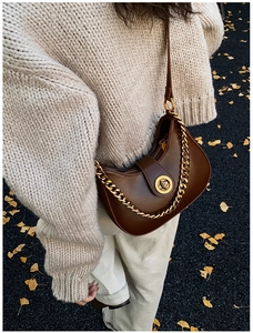 Gros plan d'un sac hobo marron avec chaîne dorée et fermoir rotatif sur pull beige