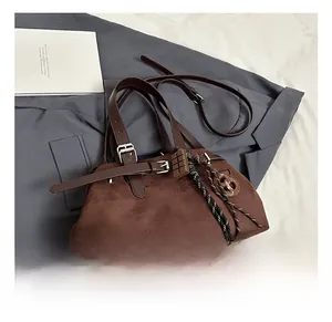 Detail of dark brown suede handbag with decorative buckle and chocolate charm on a grey blazer