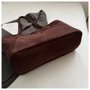 Makroaufnahme einer dunkelbraunen Wildleder-Tote-Bag mit goldenen Nieten auf Blazer