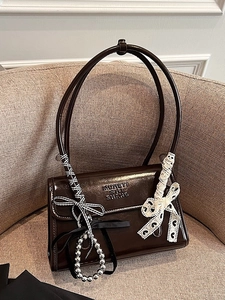 Sac bandoulière marron foncé brillant avec nœuds décoratifs sur un fauteuil