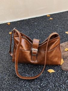 Retro brown leather shoulder bag with buckle detail on autumn ginkgo leaves background