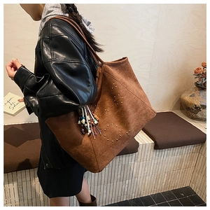 Detail der braunen Wildleder-Tote-Bag mit Metallnieten und buntem Quastenanhänger-Akzent