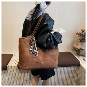 Detailansicht der braunen Wildledertasche mit Metallnieten und buntem Quastenanhänger