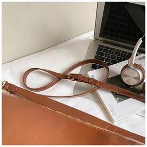 Detail of a brown leather tote bag with a gold metal buckle and adjustable strap