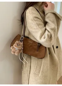 Brown suede shoulder bag with gold lettering and a cute bear pendant on a wool coat