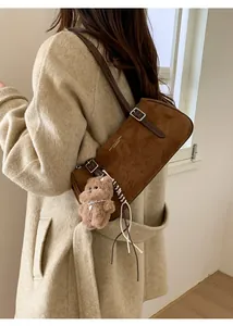 Detail of retro brown suede baguette bag with a cute teddy bear charm on shoulder
