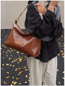 Close-up of brown leather tote bag with vintage texture and golden oval logo detail