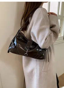 Detail of dark brown leather baguette bag with metal buckle on a shoulder model