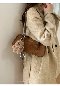 Detail of a brown suede baguette bag with a plush bear charm on an oat tweed coat