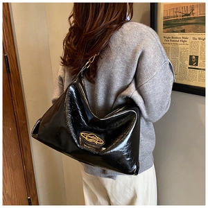 Detail of black glossy tote bag with gold logo and soft pleated design on a model
