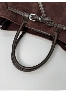 Détail d'un cabas en daim marron foncé avec poignées en cuir et ferrures en métal argenté