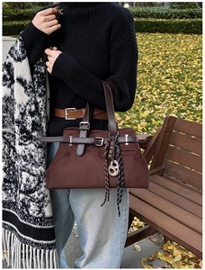 Detail of dark brown suede handbag with decorative buckle and woven pendant outdoors