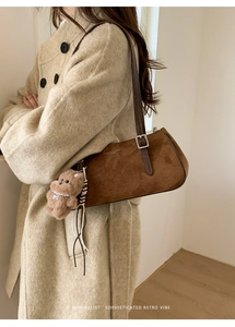 Detail of brown suede baguette bag with leather strap and plush bear charm on a model