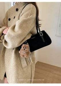 Detail of black leather shoulder bag featuring a teddy bear charm and metal buckle strap