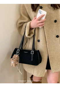 Detail of black suede shoulder bag with metallic buckle and cute plush bear charm