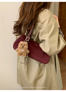 Detail view of retro burgundy suede baguette bag featuring fashion logo and plush bear charm