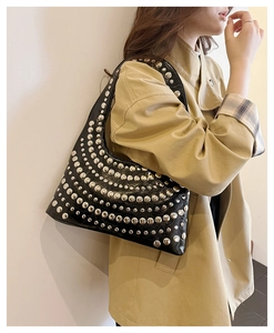 Detailansicht einer schwarzen Lackleder-Hobo-Tasche mit Nieten auf beigem Trenchcoat
