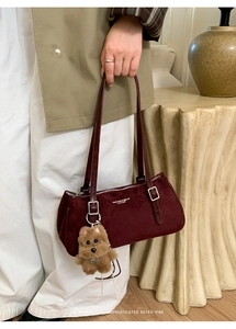 Close-up of burgundy suede baguette bag with silver hardware and plush dog charm